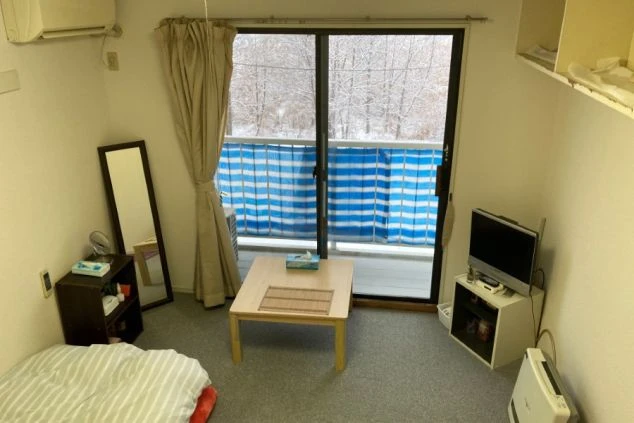 ベッド、テーブル、テレビ、エアコンが備え付けられた居室。窓の外には雪が積もった景色が広がる。