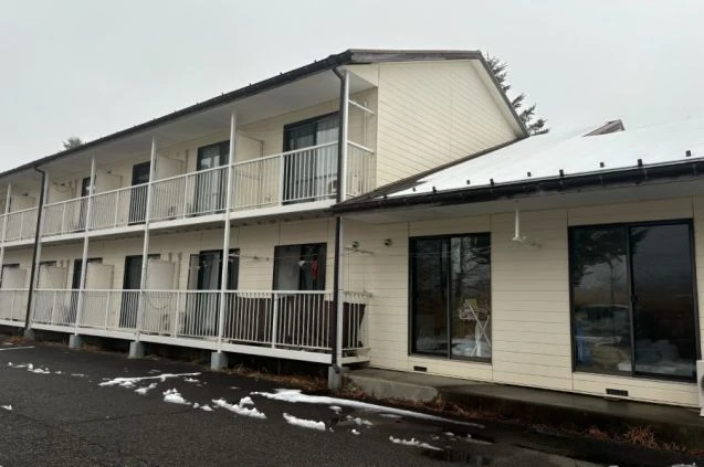 雪が部分的に積もった2階建てのアパートタイプ寮の外観。各部屋にバルコニーがある。