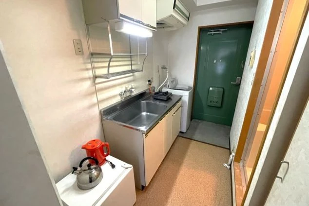リゾートバイトするスタッフが住む寮のキッチンと玄関の画像。ミニ冷蔵庫の上に電気ケトルが置いてある。