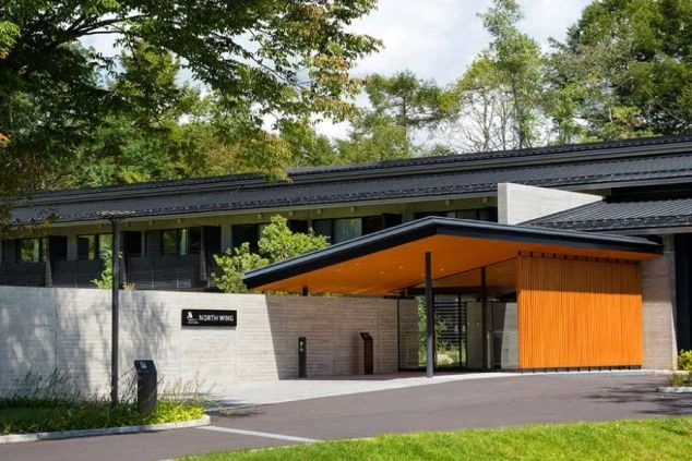 黒い屋根と木目調の壁が特徴的な、モダンなホテルの外観の画像。周りは緑の木々に囲まれており、落ち着いた雰囲気が漂っている。リゾートバイトの仕事場となる、ホテルの外観の画像。