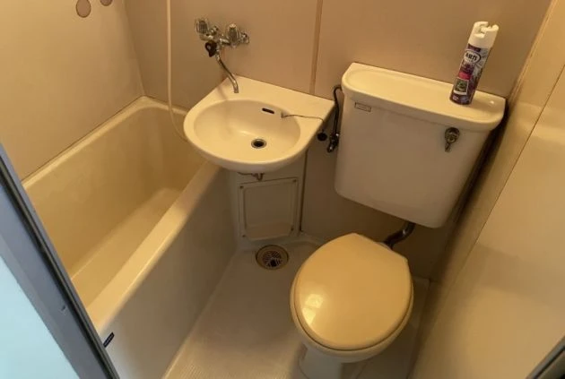 アイボリー色のバスタブと、小型の洗面台、トイレが一体となったユニットバスの内部。