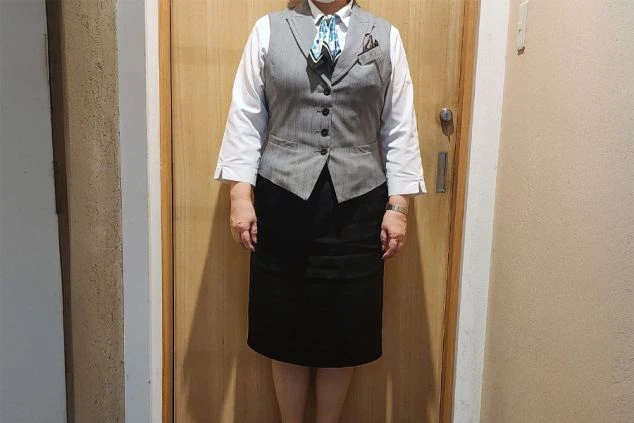 フロントで働く女性スタッフ。グレーのベストに白いシャツ、黒いスカートの制服。リゾートバイトのフロント業務の雰囲気を伝える。