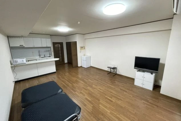 リゾートバイトで利用できるきれいな個室寮の室内。広々としたワンルームに、システムキッチン、冷蔵庫、テレビなどの家具家電が完備されている様子。