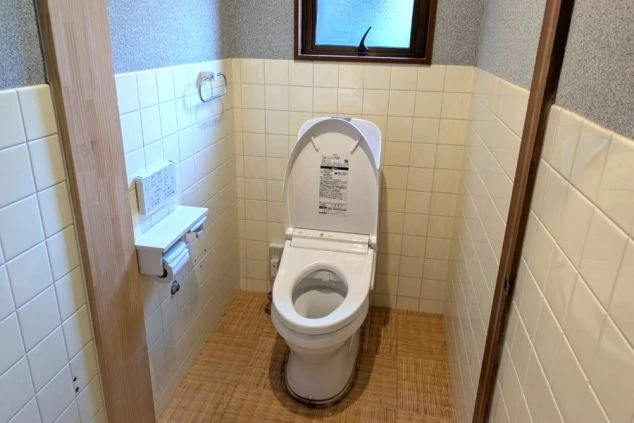 スタッフ寮個室内の清潔なトイレの画像。TOTO製の温水洗浄便座（ウォシュレット）が完備され、壁には使いやすいリモコンパネルが設置された快適な生活環境。