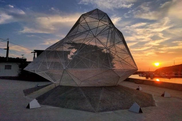 夕焼けの港に立つアート作品。日没の空とアートが広がる絶景のイメージ画像。リゾートバイトの休日を満喫。