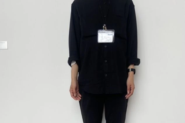 黒のシャツとパンツ、名札を着用したスタッフが映る、シンプルでモダンな制服のイメージ画像。リゾートバイトの職場の様子。