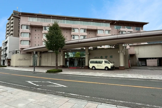 ピンクベージュの外壁の大きな建物で、庇の下にエントランス