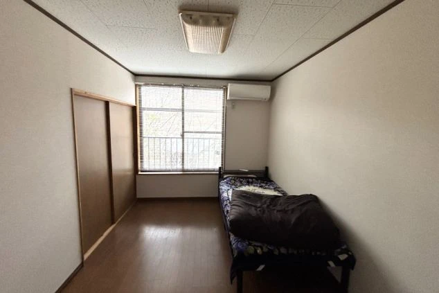 リゾートバイトの寮。シングルベッドとエアコンが完備された、シンプルで清潔感のある個室の画像。