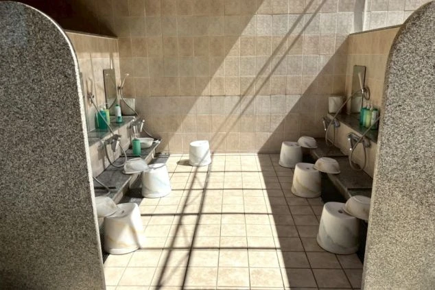 ワクトリの社員が出張で撮影した、リゾートバイトの寮にある大浴場の洗い場の画像。ベージュとグレーのタイルで清潔感があり、複数のシャワーブースと椅子、桶が並んでいる。