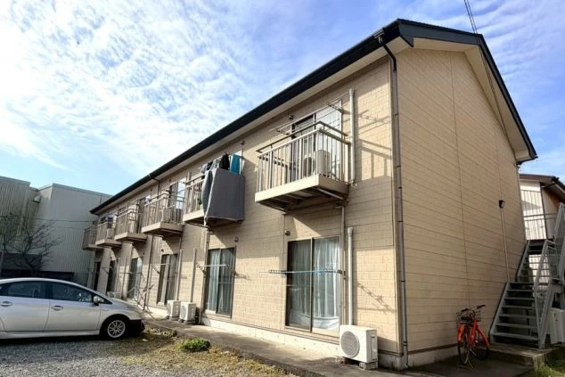 寮の外観。長い2階建ての建物で、各部屋にバルコニーがあり、駐車場は砂利敷きになっている。