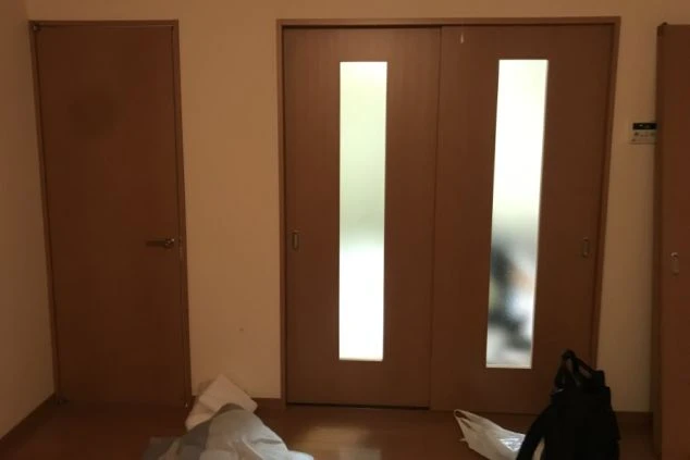 寮の居室内のドア。左側は単独のドア、右側は縦長のガラス窓が付いた引き戸(クローゼットまたは別の部屋への入り口)が二枚並んでいる。