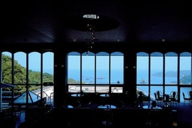 エントランスと建物外観。灰色のピラミッド型の屋根と、ベージュ色の壁、そして黒っぽい車寄せの庇（ひさし）が特徴的な建物。敷地内にはヤシの木が植えられている。