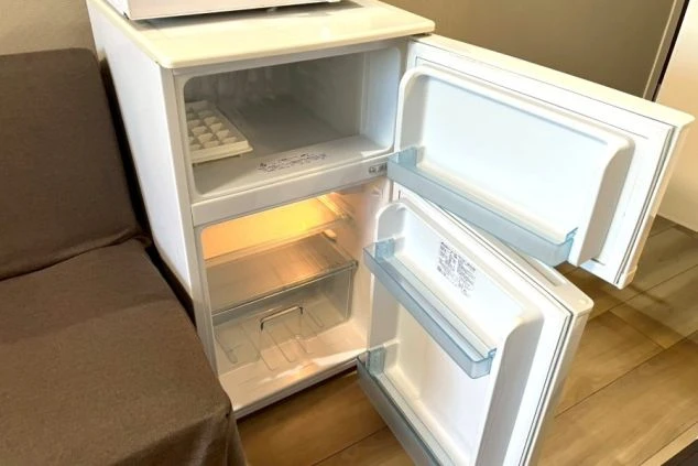 ドアが開いている小さな白い冷蔵庫。上部には冷凍庫があり、氷を作るための製氷皿が置かれている。