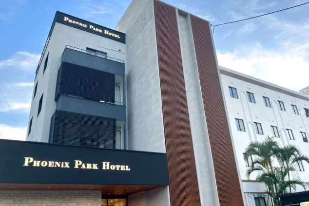 「Phoenix Park Hotel」と書かれた、白とグレーのモダンな外観のホテル。建物の前にはヤシの木がある。