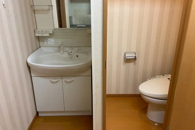 白い洗面台と、その隣に設置された温水洗浄便座付きのトイレ。壁はストライプ柄のデザイン。