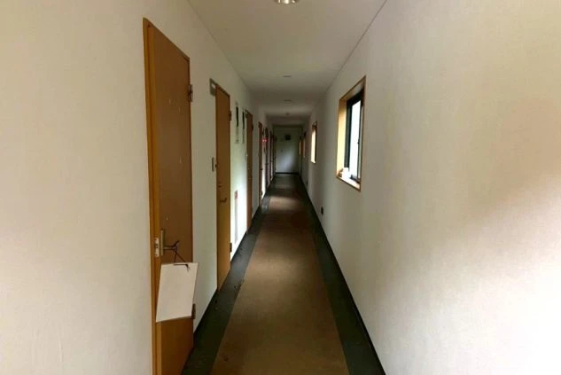 白い壁と木目調のドアが並ぶ、奥行きのある静かなアパート風の共用廊下。