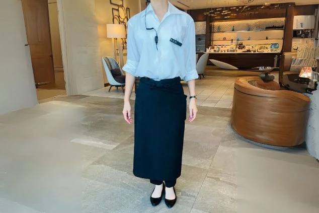 白いシャツと黒いロングエプロンを着用した、ラウンジスタッフの制服。リゾートバイトでホテル内のカフェやラウンジでの接客に興味がある方に訴求する制服の画像。