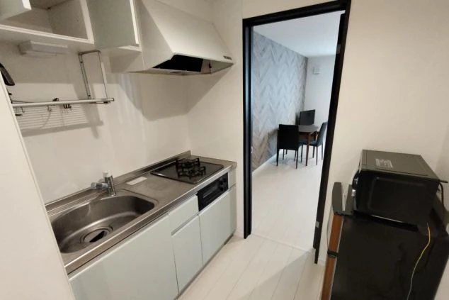 リゾートバイトの個室寮のキッチンの画像。冷蔵庫・電子レンジがあり、奥の部屋にはテーブルと椅子が見える。