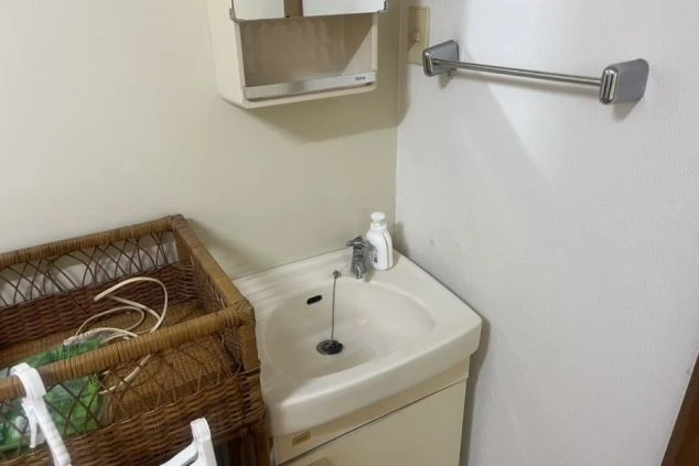 リゾートバイトの寮の洗面台の画像。鏡付きの収納棚とタオル掛けが備え付けられている。手前にはカゴが置かれ、生活感が伝わる。リゾートバイトの寮の設備の画像。