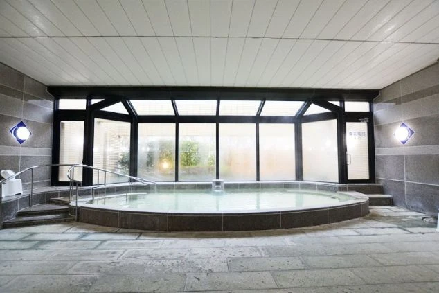 大きな窓から光が差し込む、開放的な大浴場の画像。円形の浴槽には温泉が満ちています。