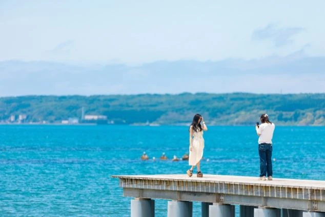 桟橋の上で写真を撮ったり、海や湖の景色を眺めたりする女性たちの写真。リゾートバイトの仕事終わりや休日に、こんな開放的で美しい景色の中でリラックスできる魅力を伝えます。