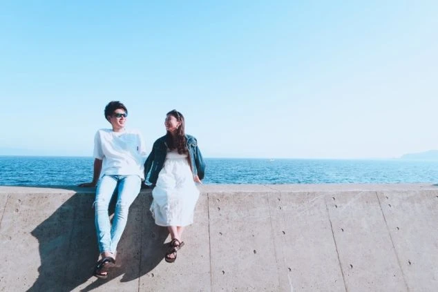 海をバックに並んで座るカップル。リゾートバイトは、カップルでの応募もOKなので、二人で最高の思い出を作れます。