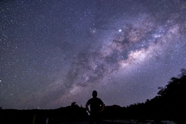 満天の星空と天の川を仰ぎ見る人物のシルエット。リゾートバイトの休日に体験できる、都会では味わえない感動的な星空観察。