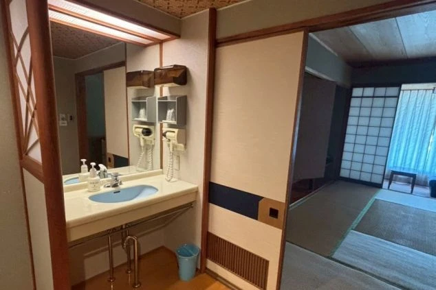 リゾートバイトの寮の洗面台と鏡を撮影した画像。ドライヤーが壁に備え付けられており、洗顔料や石鹸、アメニティグッズが置かれている。寮の部屋の洗面所の画像。