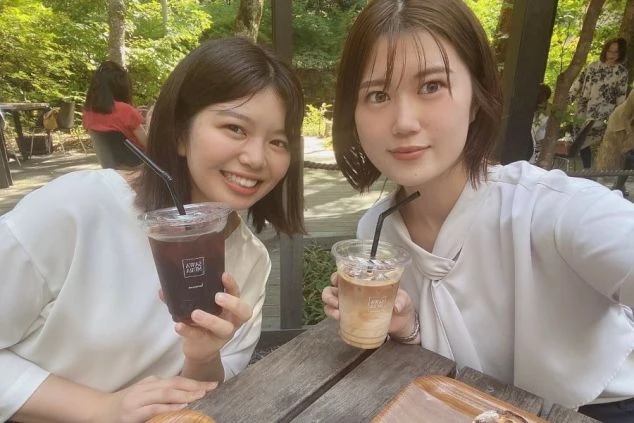 カフェのテラス席で、飲み物を持って笑顔でカメラにポーズをとる2人の女性。リゾートバイトの仕事の合間に、カフェでリフレッシュしたい方に魅力的なワクトリスタッフが撮影したオリジナル画像。