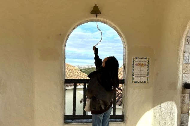 洋風のアーチ窓があるテラスで、紐を引いて「幸せの鐘」を鳴らそうとしている女性のシルエット。