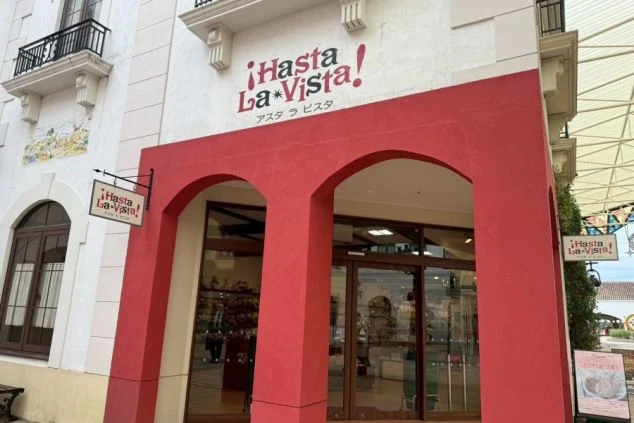 スーベニアショップ「アスタ ラ ビスタ」の外観。赤いアーチ状の入口が特徴的で、店内には多くのキャラクターグッズや土産品が並んでいるのが見えます。