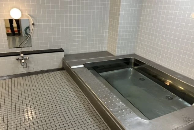 全体がタイル張りになった共用の大浴場。銀色の浴槽とシャワーがある。