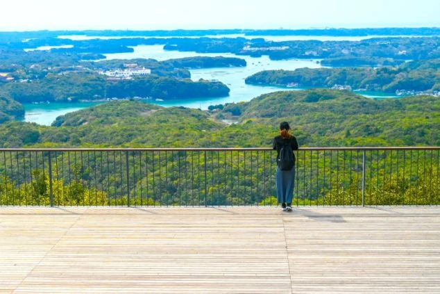 ウッドデッキの展望台から、英虞湾の浮島や入り組んだ海岸線の美しい景色を眺める人物の後ろ姿。リゾートバイト先エリアの画像。