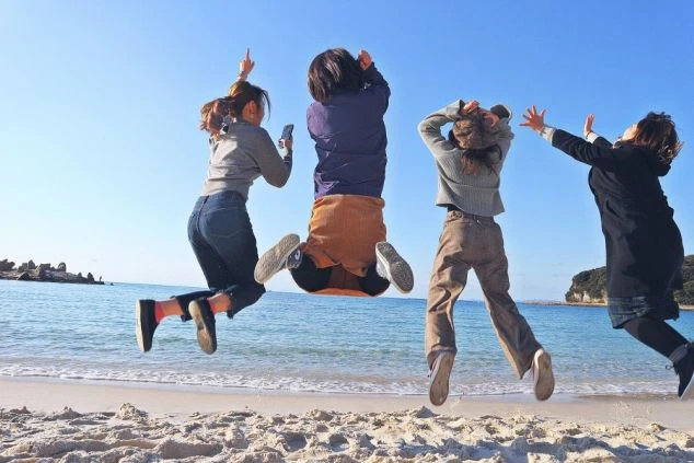 ビーチで楽しそうにジャンプする4人の若者たち。リゾートバイトの仲間との思い出作り。