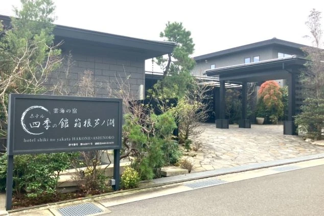 植栽と石畳に囲まれた、黒を基調としたモダンなデザインのホテルの外観。