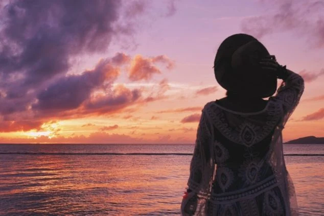 夕焼けに染まる海を眺める人物の後ろ姿の画像。オレンジと紫色の空と海が幻想的な雰囲気を醸し出し、非日常感や癒しの時間を象徴している。