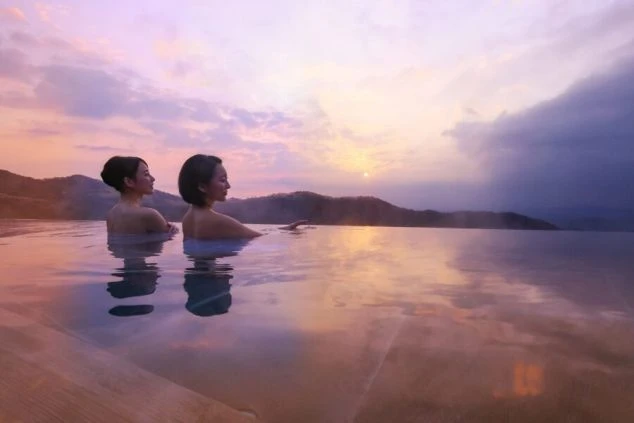 リゾートバイトの就業先の露天風呂の画像。女性2名が景色を眺めながら温泉に浸かっています。