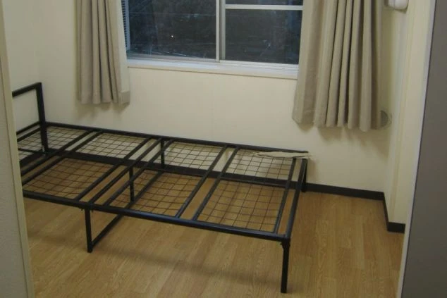 リゾートバイト寮の個室の一例。日当たりの良いフローリングのお部屋に、ベッドフレームが備え付けられています。