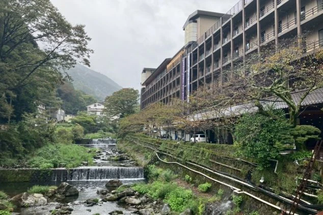 建物と、その脇を流れる渓流。川には人工的な滝（段）があり、周りは豊かな緑に囲まれている。