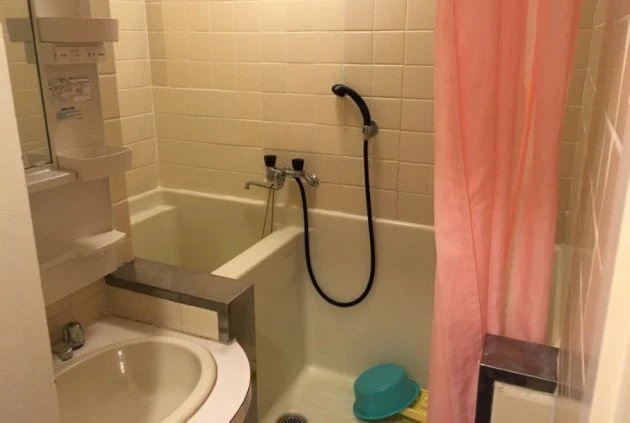 ワクトリの社員が出張で撮影した、寮のバスルームの画像。浴槽とシャワー、そして洗面台が一体となったユニットバスで、ピンクのシャワーカーテンが設置されている。