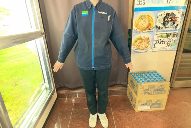 ファミリーマートの制服を着用したスタッフの画像。紺色のジャケットに青いファスナー、黒いズボンを着用している。リゾートバイトの仕事内容の一つである、売店・コンビニスタッフの制服の画像。