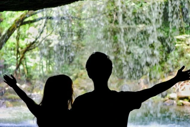 軽井沢の滝を背景に、手を広げて景色を眺める2人の人物のシルエットの画像。緑豊かな自然の中での開放感や、リゾートバイトで得られる非日常的な体験を表現している。