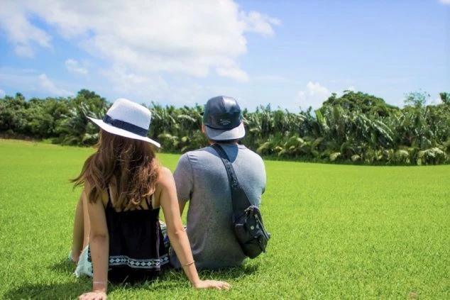 晴れた日の広い草原にカップルが並んで座っている画像。自然を五感で感じながらゆっくり過ごしている。カップルでリゾートバイトをした時の休日の過ごし方の一例。