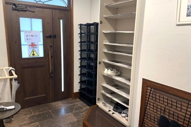 リゾートバイトの女子寮の玄関の画像。木製のドアの横には、靴箱とシューズラックが設置されており、整理整頓された状態。寮の共用スペースとして、快適な生活環境を保つための配慮が感じられる。