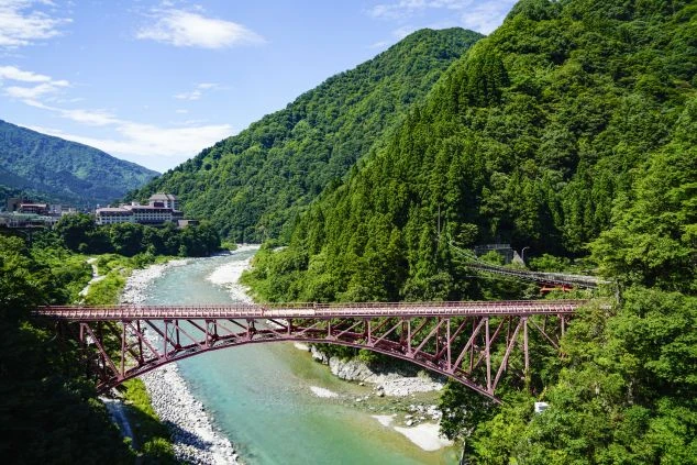 深い緑の山々とエメラルドグリーンの川に架かる赤い鉄橋。富山県の自然豊かな場所でのリゾートバイトで、絶景を楽しみながら働こう。