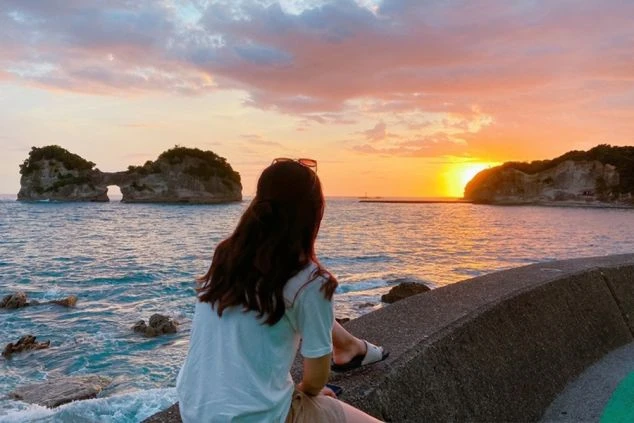 和歌山県南紀白浜の海沿いでリゾートバイトする人若い女性が黄昏る後ろ姿の画像