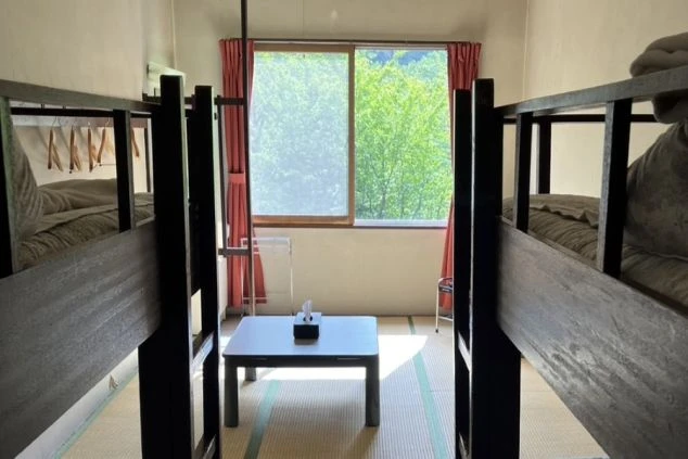 リゾートバイト先の相部屋寮の部屋全体の画像。二段ベッドが2つと畳の共用スペースがあります。