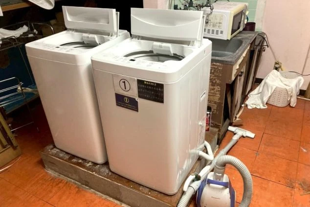 スタッフ寮内のランドリースペース。2台の縦型洗濯機が並び、右奥には流し台と電子レンジがある。