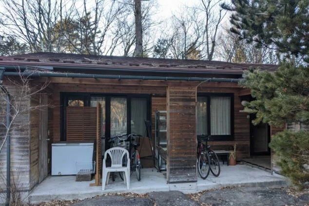 木造の平屋建てリゾートバイト寮の外観。各部屋の玄関前には自転車や私物が置かれており、生活感のある雰囲気が伝わる。生活に便利な設備が整った個室寮をアピール。