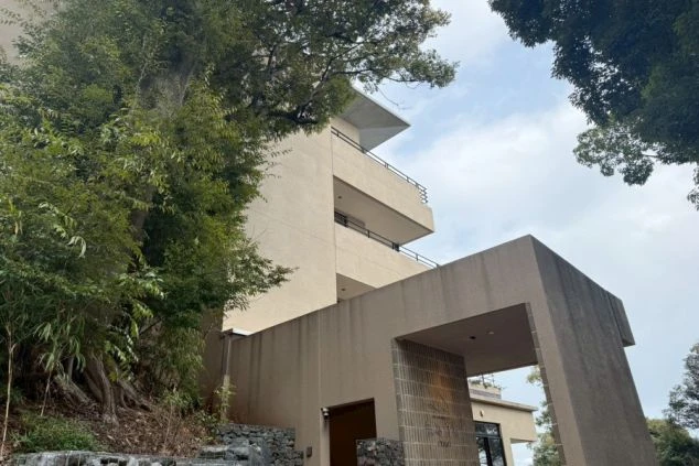 木々に囲まれたモダンな建物の外観と、手前に広がる豊かな緑。